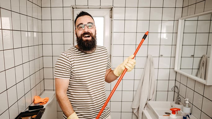 Man holding a mop while cleaning the bathroom wants to learn some bathroom cleaning hacks. 