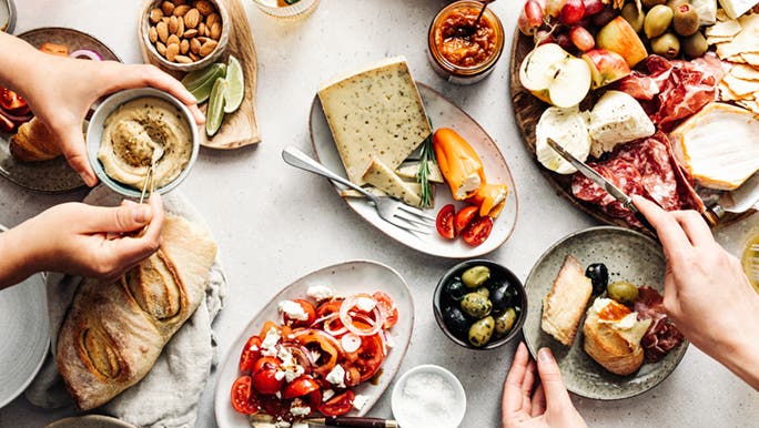 A platter of Mediterranean mood boosting foods is laid out on a table, with people serving themselves.