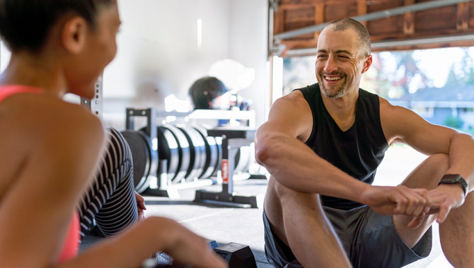 Husband and wife sit on the floor after a workout in their home gym in the garage