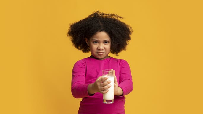 A young girl is holding onto a glass of milk, she seems frustrated to know that her farts smell really bad, from the constant milk she’s been having.