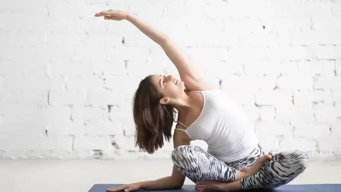 Woman in side bend pose on a dark yoga mat in a white studio