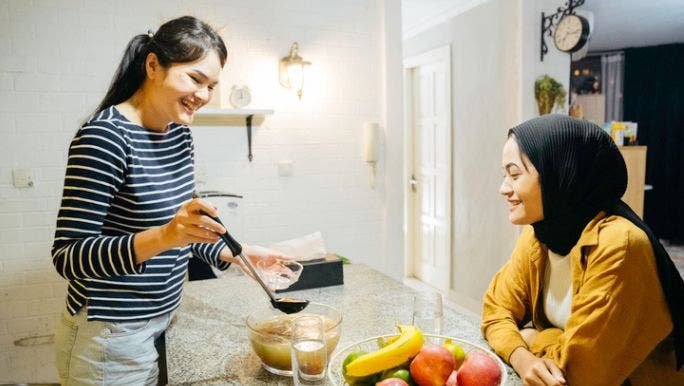 Two Asian women are in a kitchen laughing and eating bone broth