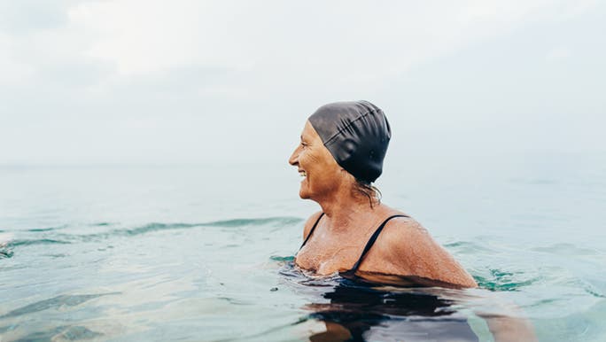 Lady wearing black swimmers and swimming cap enjoying the ocean. She is developing the healthy habit of daily exercise.