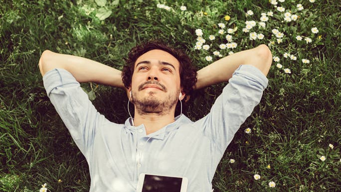 Lying in the grass with his head resting on his arms, a man calmly smiles and wonders whether affirmations work.
