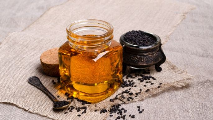 A small pot of black seeds is sitting on a table beside a jar of honey