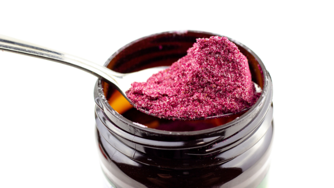A spoon full of beetroot powder above an open jar