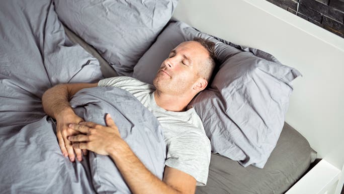 A man is sleeping on his back in a bed made with grey linen