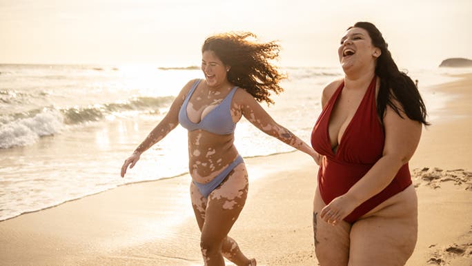 Two young women walking on the beach and laughing, which may be considered important when it comes to fertility and fitness