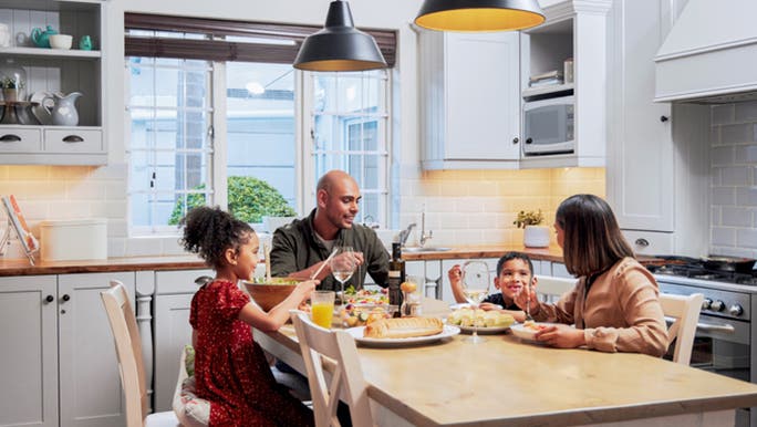 A young family of four is sitting at the kitchen table enjoying a meal together