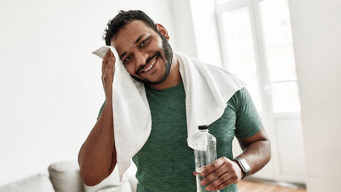 A man dries his sweaty face with a white towel. He has been working out at home. 