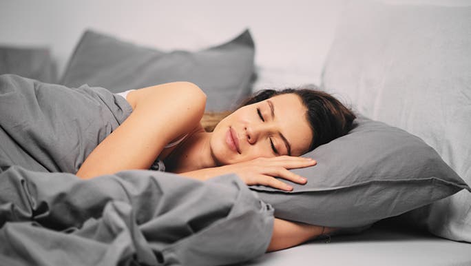 A brunette woman is having a peaceful sleep in a bed made with grey linen