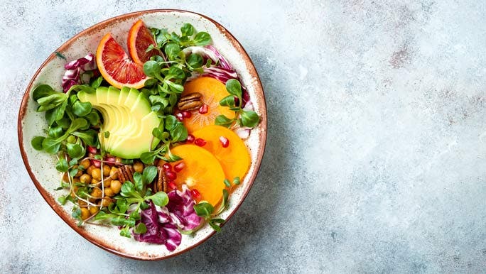 Vegan, detox Buddha bowl with turmeric roasted chickpeas, greens, avocado, persimmon, blood orange, nuts and pomegranate