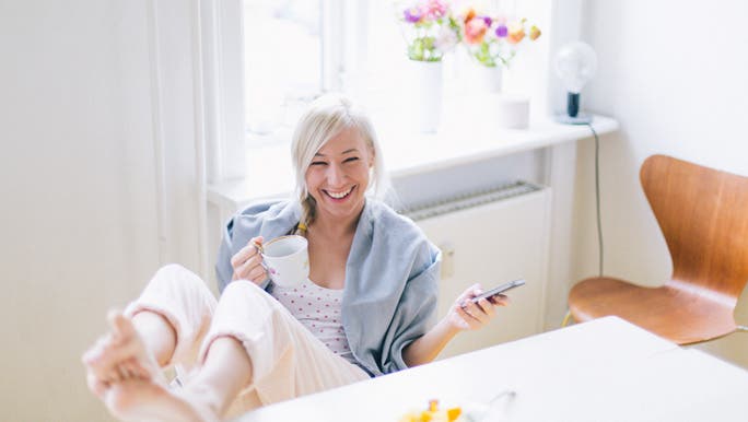 Young woman using a mobile phone while having healthy breakfast