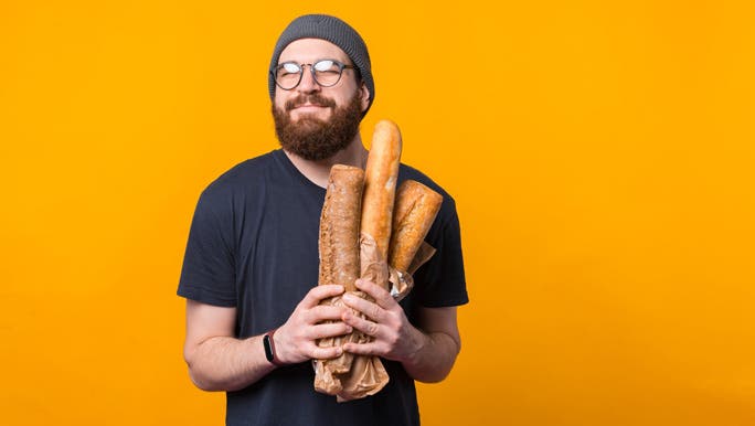 Smiling bearded man holding a bag of bread in front of an orange background
