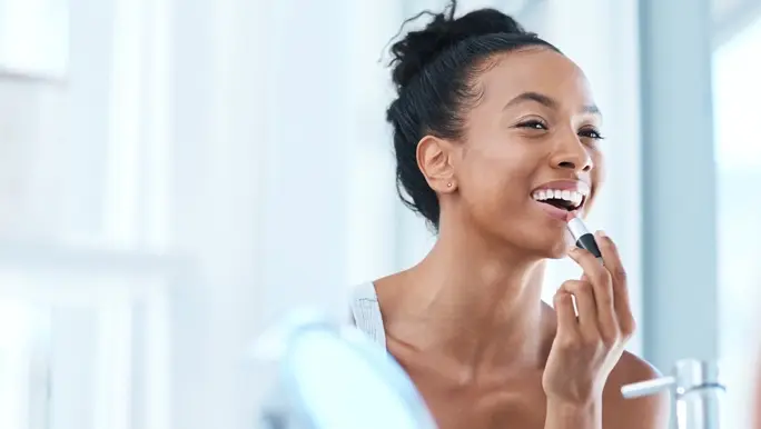 Woman with black hair in a bun applying natural lipstick in the mirror