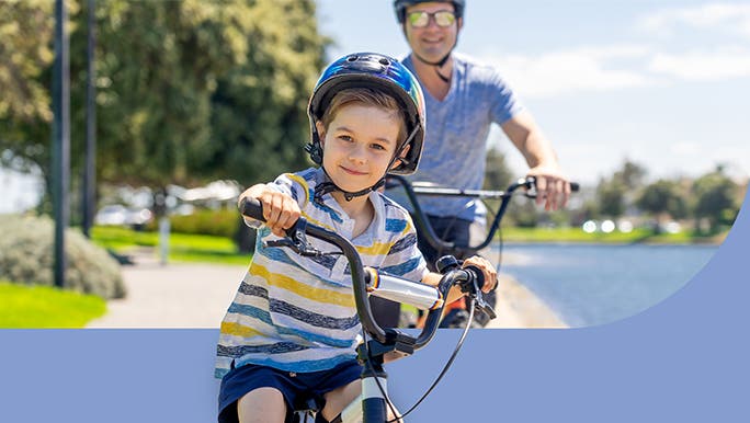 A young boy is riding bikes with his dad in the park