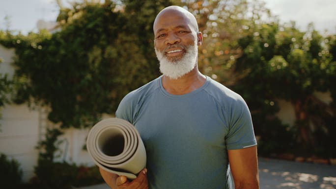 A man stands with a yoga mat under his arm.