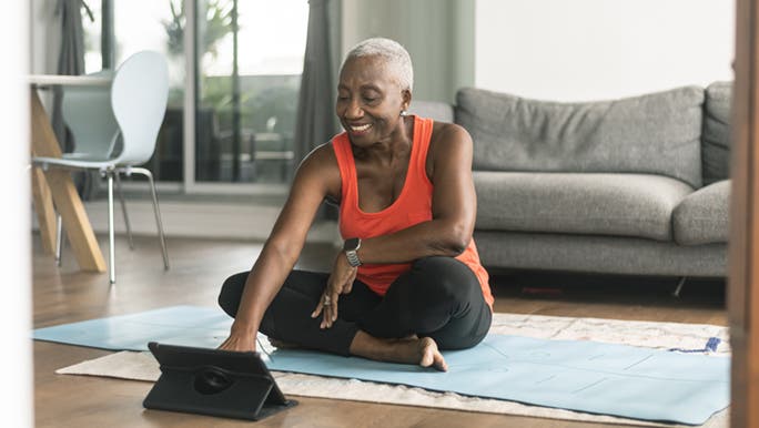A woman sitting on her yoga mat in the lounge room is smiling while looking at her tablet as she has found the best free yoga online.