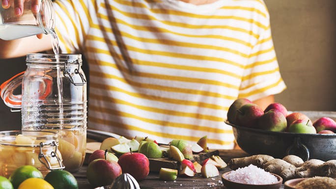 Image of a woman’s torso as she makes homemade apple cider vinegar with piles of apples on a table