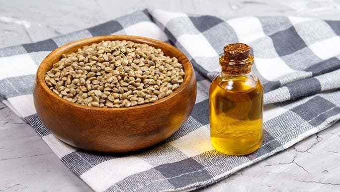 Hemp seed in a wooden bowl sits next to a bottle of hemp seed oil to represent the benefits of hemp seed. 