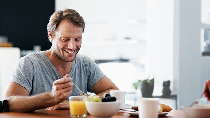 A man is eating a well balanced meal at his dining table. He is smiling because he knows eating well is how you can clear up adult acne.