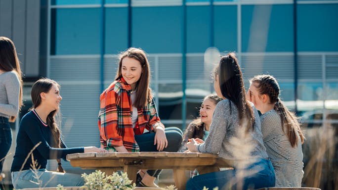 Five teenage girls sitting at a table on a sunny winter day discussing teenage crushes. 