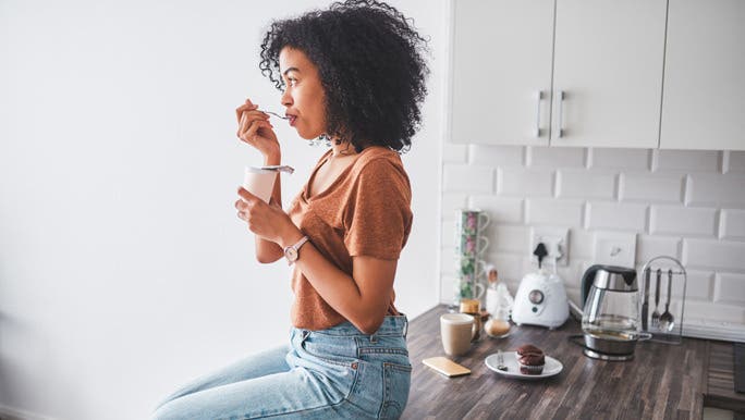 Young woman sitting on the kitchen bench eating probiotic rich yoghurt
