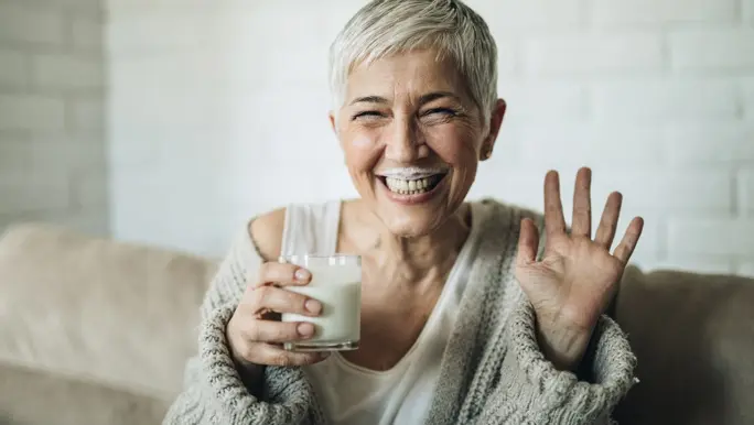 Happy woman with short grey hair drinking soy milk and laughing with a milk moustache