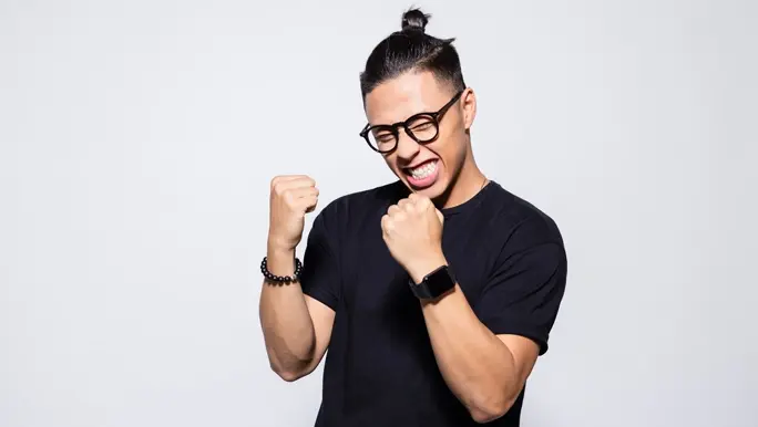 Happy young man in a black t-shirt and glasses clenching his fists