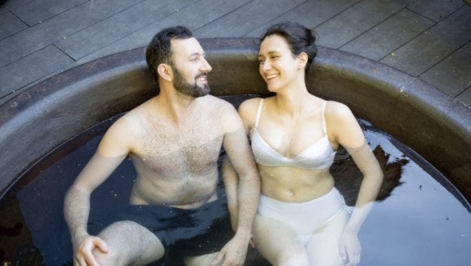 A young Caucasian couple are sitting in an ice bath and smiling