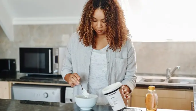 Woman at home in the kitchen spooning yoghurt into a bowl
