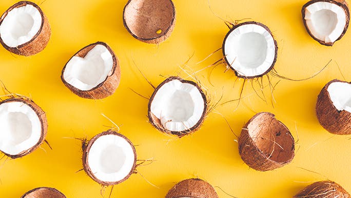 On a yellow background, coconuts that have been cut in half are displayed in a pattern. 