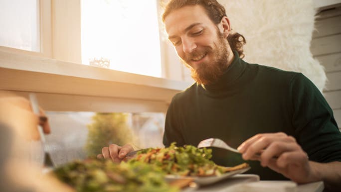 A man smiles as he sits at a table about to eat a meal because he knows the best sources of iron for vegetarians. 
