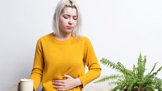 Woman sitting on the floor with a mug holding her stomach thinking