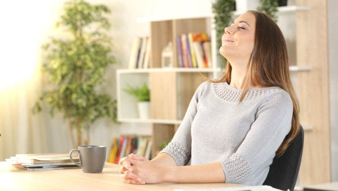 A young woman is sitting a desk with her eyes closed and practising breathing exercises