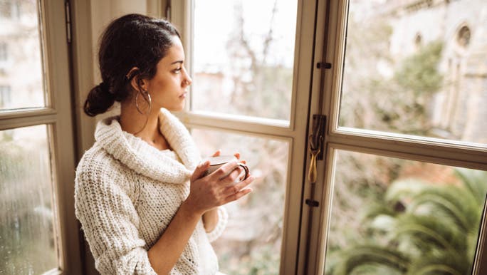 Young woman holding a mug of tea, gazing out the window