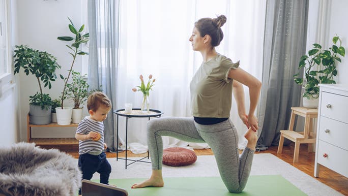 A mother does a virtual yoga class from her lounge room, with her toddler playing next to her. Perhaps her child is her motivation to lose weight and workout. 