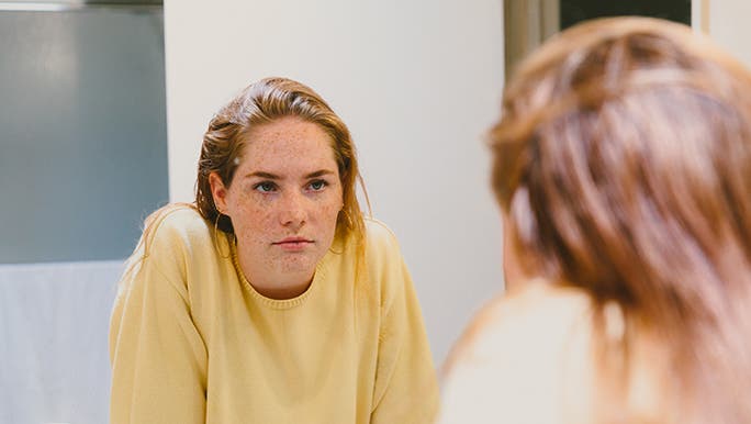 A young woman stared at her reflection in the mirror with a neutral expression on her face. 