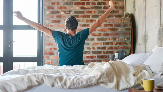 Rear view of young man stretching hands in bed. Male is waking up in the morning. He is relaxing at home.