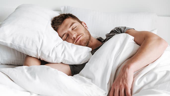A young man is sleeping peacefully in a bed made with white linen