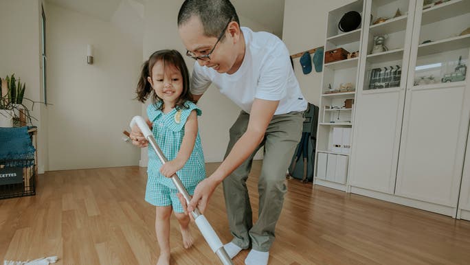 An asian man and a young Asian girl are mopping a timber floor together