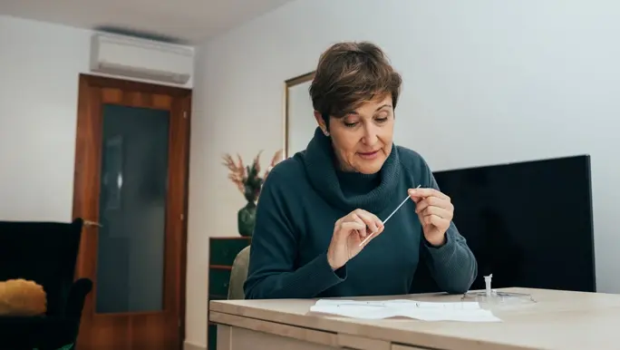  Senior woman sitting at home, studying the instructions for a home rapid antigen COVID-19 test 