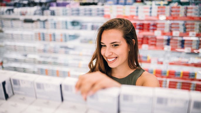 A woman smiles as she chooses a menstruation product off a chemist shelf. 