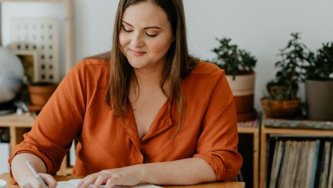 A young woman is smiling as she writes positive affirmations in a journal