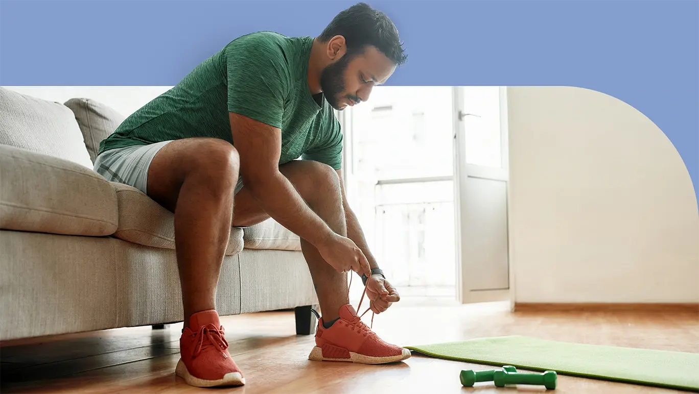 Man sitting on the couch tying up his shoelaces and getting ready to exercise
