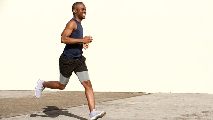 A man is smiling while running as he is enjoying the benefits of HIIT.