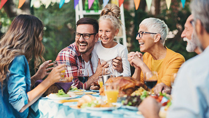Family laughing around an outdoor lunch table 