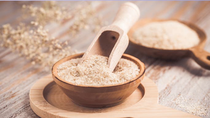 On a wooden bench, a bowl of psyllium husk sits with a wooden scoop, as good prebiotic food choice