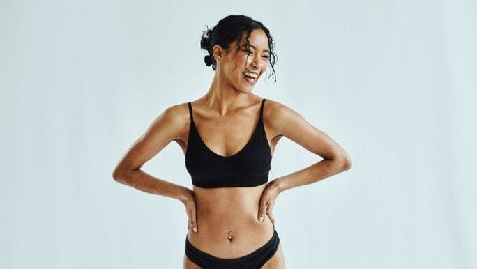 A young Asian woman is smiling and wearing black underwear as she holds her hands on her hips