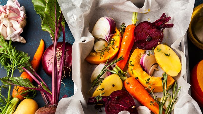 From above, a bunch of veggies are in a roasting pan and on the table next to it. Vegetables are some of the best foods for gut health. 